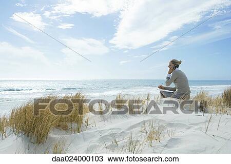 Woman sitting on dunes at beach, using cell phone View Large Photo Image Stock Image - Woman sitting on dunes at beach, using cell phone. Fotosearch