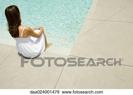 Stock Photo - Woman sitting on edge of pool, rear view. Fotosearch