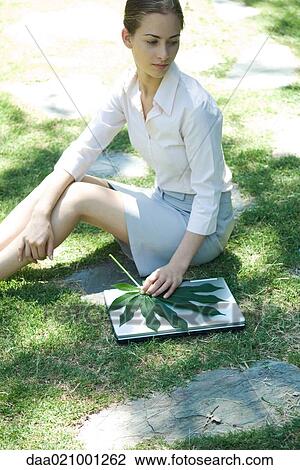 Woman sitting on grass, holding leaf on top of laptop View Large Photo Image Stock Image - Woman sitting on grass, holding leaf on top of laptop. Fotosearch