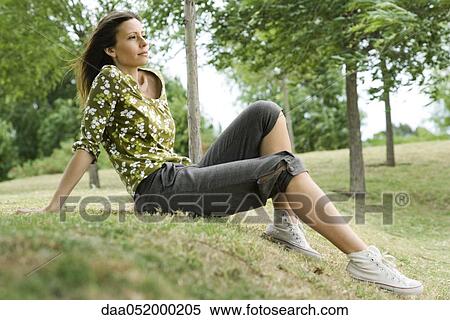 Stock Photography - Woman sitting on grass in park, looking away in thought. Fotosearch