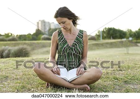 Woman sitting on grass, reading book View Large Photo Image Picture - Woman sitting on grass, reading book. Fotosearch