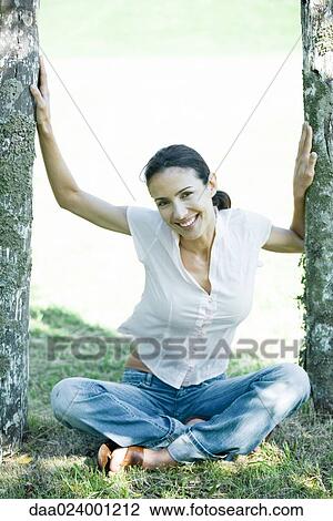 Stock Image - Woman sitting on ground between wooden posts, smiling at camera. Fotosearch