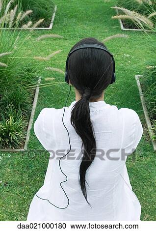 Woman sitting on landscaped lawn, rear view, listening to headphones View Large Photo Image Stock Image - Woman sitting on landscaped lawn, rear view, listening to headphones. Fotosearch