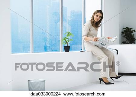 Woman sitting on ledge, holding newspaper, smiling at camera View Large Photo Image Picture - Woman sitting on ledge, holding newspaper, smiling at camera. Fotosearch
