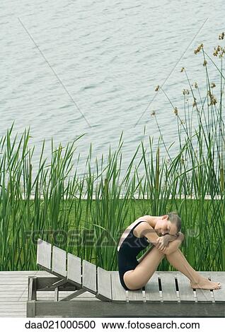 Woman sitting on lounge chair next to lake, hugging knees, resting head on arms View Large Photo Image Stock Image - Woman sitting on lounge chair next to lake, hugging knees, resting head on arms. Fotosearch