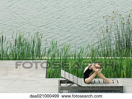 Woman sitting on lounge chair next to lake, hugging knees, resting head on arms View Large Photo Image Stock Photo - Woman sitting on lounge chair next to lake, hugging knees, resting head on arms. Fotosearch