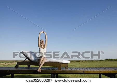 Woman sitting on lounge with arms stretched above head View Large Photo Image Stock Photo - Woman sitting on lounge with arms stretched above head. Fotosearch