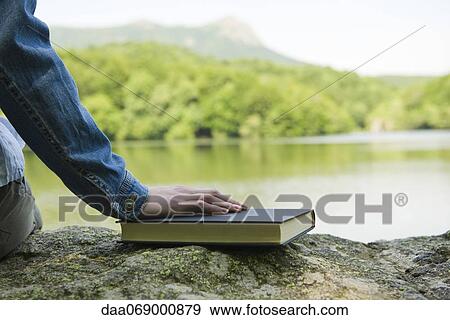 Woman sitting on rock by lake with book, cropped View Large Photo Image Stock Photo - Woman sitting on rock by lake with book, cropped. Fotosearch