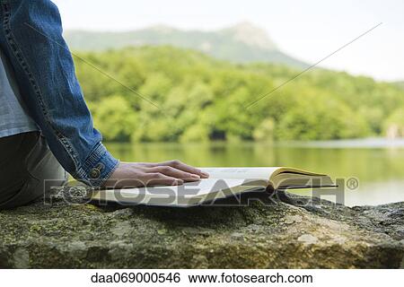 Woman sitting on rock by lake with book, cropped View Large Photo Image Stock Photograph - Woman sitting on rock by lake with book, cropped. Fotosearch