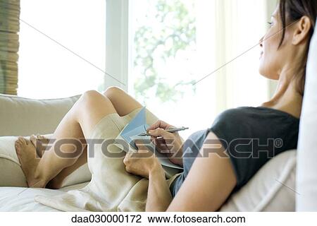 Woman sitting on sofa, holding stationery and pen View Large Photo Image Stock Image - Woman sitting on sofa, holding stationery and pen. Fotosearch