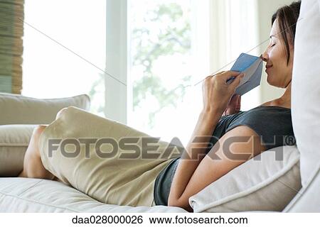 Woman sitting on sofa, holding up card and envelope to nose, smiling with eyes closed View Large Photo Image Stock Photograph - Woman sitting on sofa, holding up card and envelope to nose, smiling with eyes closed. Fotosearch