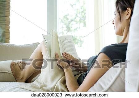 Woman sitting on sofa with feet up, reading View Large Photo Image Stock Image - Woman sitting on sofa with feet up, reading. Fotosearch