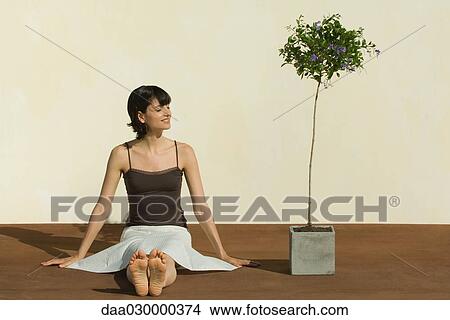 Picture - Woman sitting on the ground beside potted plant, smiling, eyes closed. Fotosearch