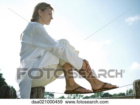 Stock Photo - Woman sitting on top of fence, low angle view. Fotosearch