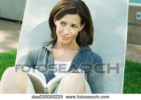 Stock Photography - Woman sitting outdoors, holding open book, looking away. Fotosearch