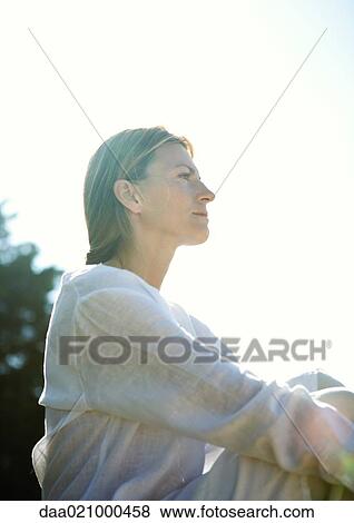 Woman sitting outdoors, low angle view View Large Photo Image Stock Photo - Woman sitting outdoors, low angle view. Fotosearch