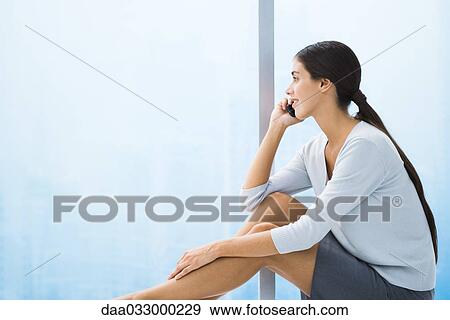 Woman sitting with legs up, talking on cell phone, looking out window View Large Photo Image Stock Photo - Woman sitting with legs up, talking on cell phone, looking out window. Fotosearch
