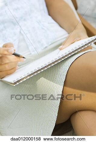 Woman sitting with pencil and notepad on lap, close-up View Large Photo Image Stock Photo - Woman sitting with pencil and notepad on lap, close-up. Fotosearch
