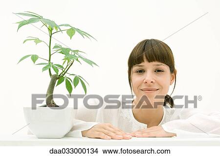 Woman sitting with potted plant, smiling at camera View Large Photo Image Picture - Woman sitting with potted plant, smiling at camera. Fotosearch