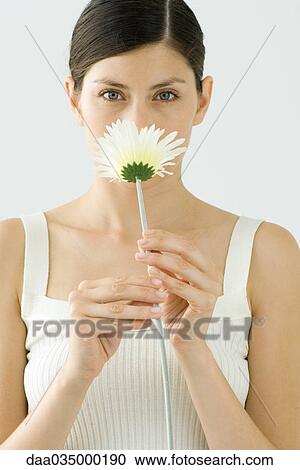 Stock Image - Woman smelling gerbera daisy, portrait. Fotosearch