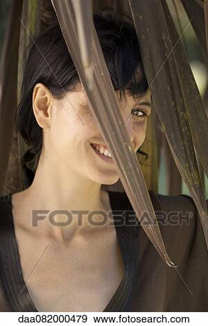 Woman smiling through foliage, portrait View Large Photo Image Stock Photo - Woman smiling through foliage, portrait. Fotosearch