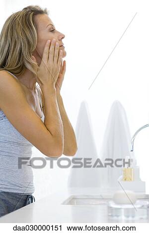 Woman standing at bathroom sink, touching face, looking at self View Large Photo Image Stock Image - Woman standing at bathroom sink, touching face, looking at self. Fotosearch