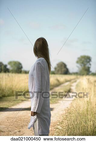 Woman standing at edge of rural road, looking away View Large Photo Image Stock Image - Woman standing at edge of rural road, looking away. Fotosearch