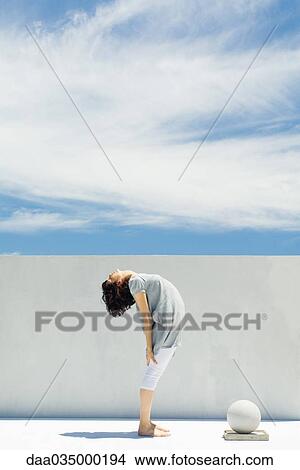 Picture - Woman standing, bending backwards, fitness ball nearby. Fotosearch