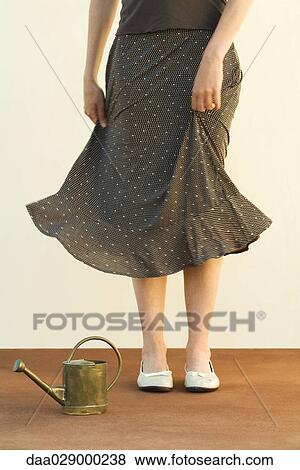 Woman standing beside watering can, holding skirt, cropped view View Large Photo Image Stock Photo - Woman standing beside watering can, holding skirt, cropped view. Fotosearch