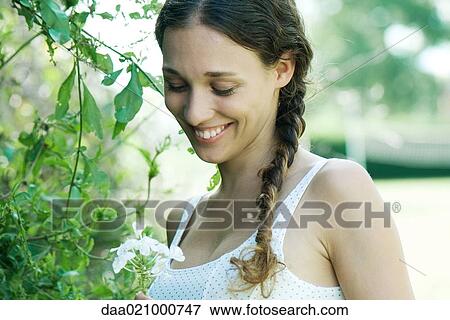 Stock Photo - Woman standing by flowering tree, smiling, looking down. Fotosearch