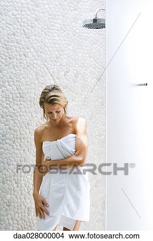 Picture - Woman standing by shower, wrapped in towel, looking down. Fotosearch