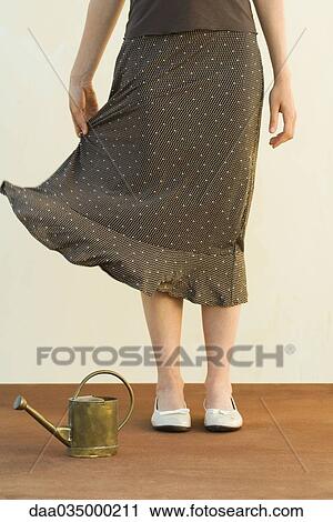 Stock Image - Woman standing by watering can, holding skirt, cropped view. Fotosearch