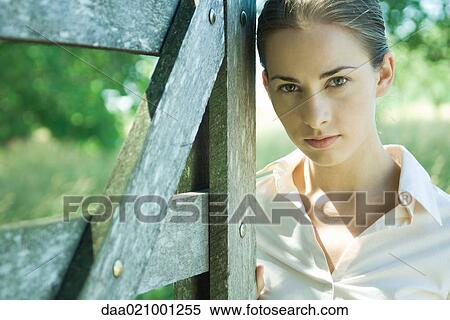 Stock Photography - Woman standing by wood gate, looking at camera. Fotosearch