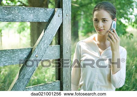 Woman standing by wood gate, using cell phone View Large Photo Image Stock Photograph - Woman standing by wood gate, using cell phone. Fotosearch