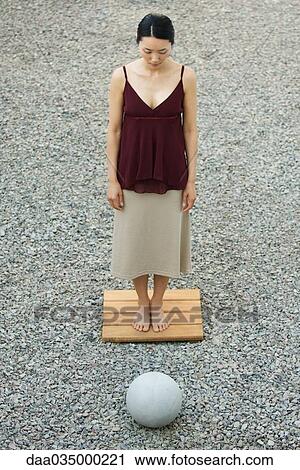 Stock Image - Woman standing, facing sphere in rock garden, high angle view. Fotosearch