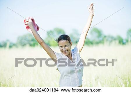 Woman standing in field, arms in air, smiling at camera View Large Photo Image Picture - Woman standing in field, arms in air, smiling at camera. Fotosearch