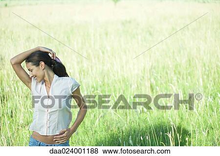 Woman standing in field, one hand on head, the other on hip, smiling View Large Photo Image Stock Photo - Woman standing in field, one hand on head, the other on hip, smiling. Fotosearch