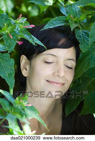 Woman standing in lush foliage, eyes closed, smiling View Large Photo Image Stock Photo - Woman standing in lush foliage, eyes closed, smiling. Fotosearch