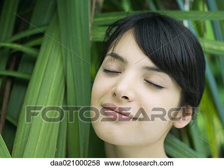 Woman standing in lush foliage, eyes closed, smiling View Large Photo Image Stock Photo - Woman standing in lush foliage, eyes closed, smiling. Fotosearch