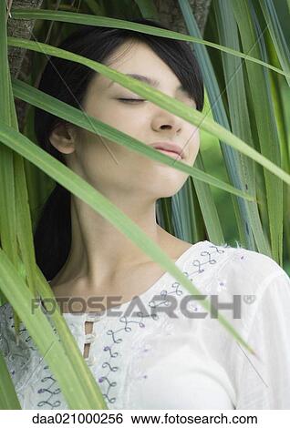 Woman standing in lush foliage, eyes closed, smiling View Large Photo Image Stock Photograph - Woman standing in lush foliage, eyes closed, smiling. Fotosearch