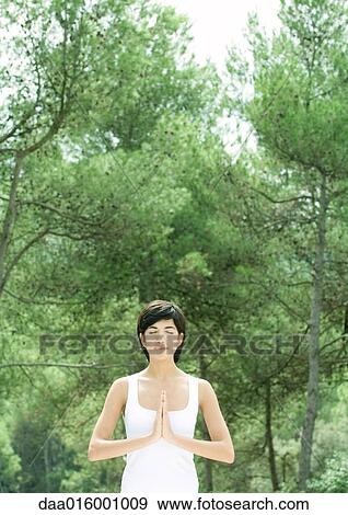 Stock Photo - Woman standing in prayer position, trees in background. Fotosearch