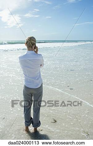 Woman standing in surf, using cell phone, rear view View Large Photo Image Stock Image - Woman standing in surf, using cell phone, rear view. Fotosearch