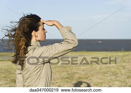 Stock Photo - Woman standing in wind looking at the sea. Fotosearch