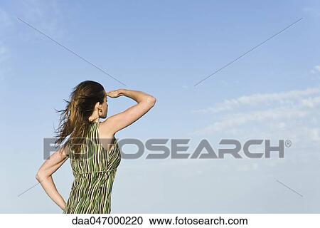 Woman standing in wind with hand shading eyes, sky in background View Large Photo Image Stock Image - Woman standing in wind with hand shading eyes, sky in background. Fotosearch