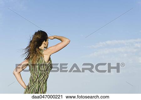 Woman standing in wind with hand shading eyes, sky in background View Large Photo Image Stock Image - Woman standing in wind with hand shading eyes, sky in background. Fotosearch