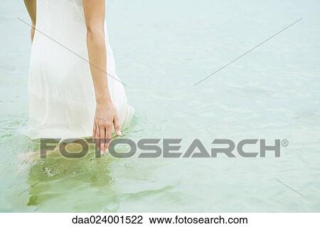 Woman standing knee deep in ocean, touching surface of water, cropped View Large Photo Image Stock Image - Woman standing knee deep in ocean, touching surface of water, cropped. Fotosearch
