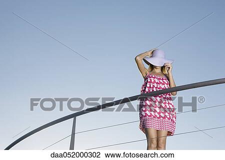 Woman standing on balcony, covering face with sun hat View Large Photo Image Stock Image - Woman standing on balcony, covering face with sun hat. Fotosearch