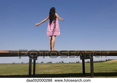 Stock Photo - Woman standing on deck with arms out, rear view. Fotosearch