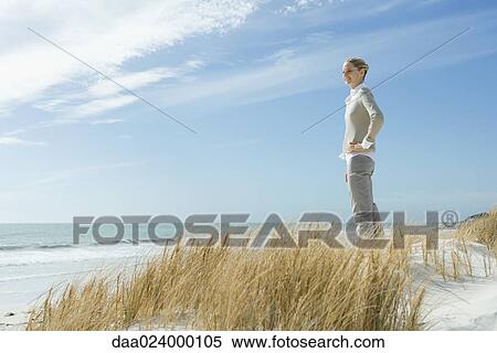 Stock Photography - Woman standing on dune, looking into distance, smiling. Fotosearch
