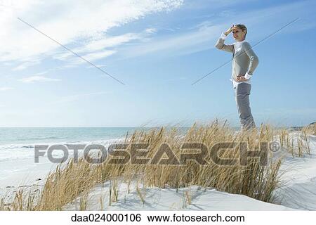 Woman standing on dune, shading eyes and looking into distance, smiling, full length View Large Photo Image Stock Photograph - Woman standing on dune, shading eyes and looking into distance, smiling, full length. Fotosearch
